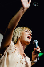 a woman singing into a microphone praising God 