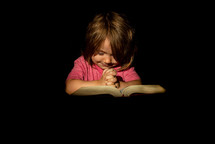 A girl praying with her hands on a Bible.