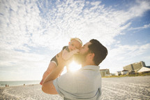 a father kissing his infant daughter on a beach 