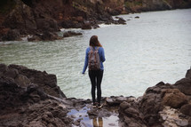 teen girl looking out at the ocean standing on a shore 