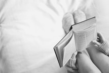 a girl sitting on a bed reading a Bible 