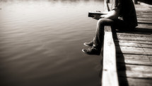 A young adult, white man, sitting at the edge of a dock reading his Bible