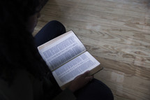 a woman looking down reading the pages of a Bible 
