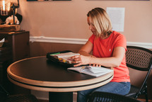 a woman sitting at a table reading a Bible 
