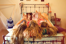 three sisters lying on a bed looking at a magazine 