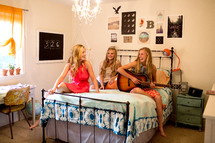 three sisters sitting on a bed playing a guitar and singing 