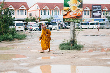 a monk in a orange robe cross a parking lot 