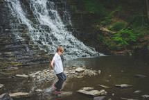 a boy walking across rocks in a stream