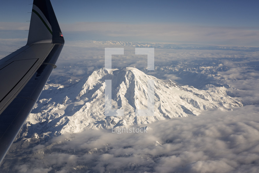a plane wing flying over a snow capped mountain 