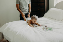 a father pulling a toddler by his feet on a bed 