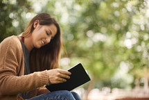 a woman sitting on a park bench reading a Bible