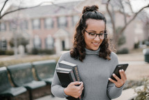 a young woman holding a cellphone and a stack of books 