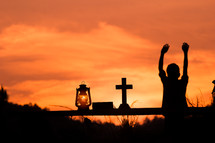 a child with hands raised and oil lamp, Bible, and cross at sunset 