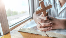 Close up hands of boy holding christian cross and praying on Holy Bible