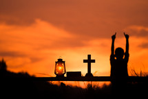 a child with hands raised and oil lamp, Bible, and cross at sunset 