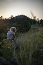 a little girl sitting outdoors in a field 