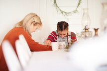 mother and daughter praying together at a table in the home