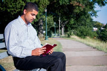 man sitting on a bench reading a Bible 