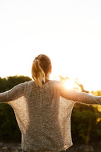a woman standing outdoors at sunset with outstretched arms 