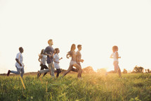 young adults running through a field at sunset 