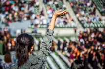 a woman in the audience with a raised hand at a graduation ceremony. 
