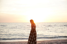 a woman walking on a beach in a dress at sunset 