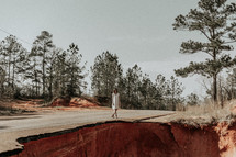 a woman standing at the edge of a collapsed road 