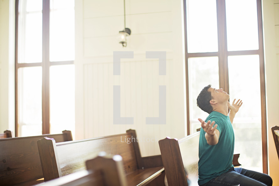 Man with arms extended while praying in a church pew.