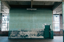 A large empty room with old walls and a green door.