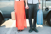 a couple standing in front of a van holding suitcases 