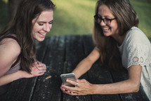 teen girls looking at a cellphone screen sitting at a picnic table 