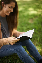 a woman reading a Bible sitting in the grass 
