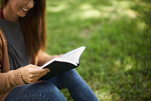 a woman sitting in grass reading a Bible 