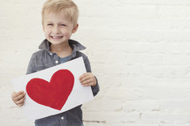 toddler boy happily holding a painting of a heart 