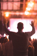 a man standing with raised hands at a concert 
