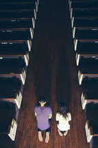 Couple praying on their knees in the aisle in a dark, empty church.