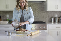 A woman pouring pie filling into a prepared pie crust.