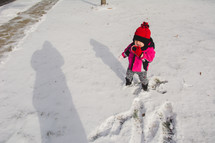 A toddler iicks snow in a snow covered yard in winter