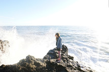 girl standing on rocks with waves splashing her 