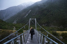a woman walking over a swinging bridge 