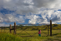 toddler girl standing at a ranch gate 