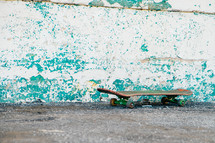 Skateboard on the pavement by a weathered wall.