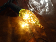 Close up of large yellow tree light bulb with reflections against dark wall