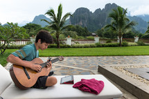 boy playing a guitar near palm trees 
