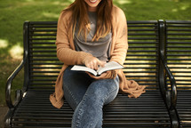 a woman sitting on a park bench reading a Bible in fall 