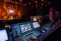 a man controlling the lights and sound behind a soundboard at a concert 