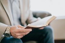 a man in a suit sitting reading a Bible 