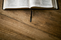 edge of an open Bible lying on a wood table