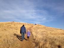 a father and daughter walking up a hill holding hands 