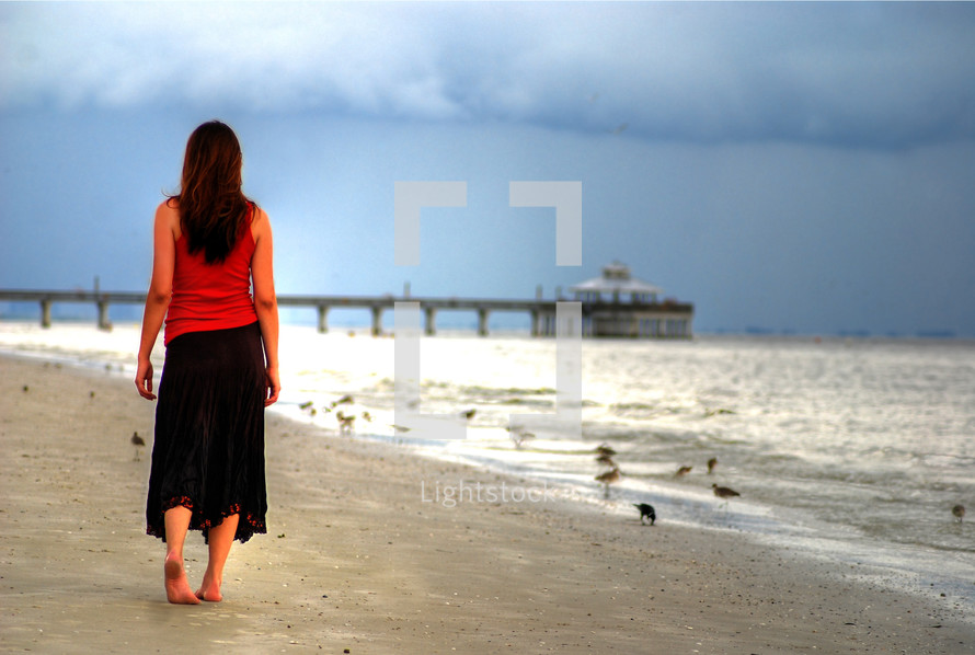 woman walking on a beach towards a pier 